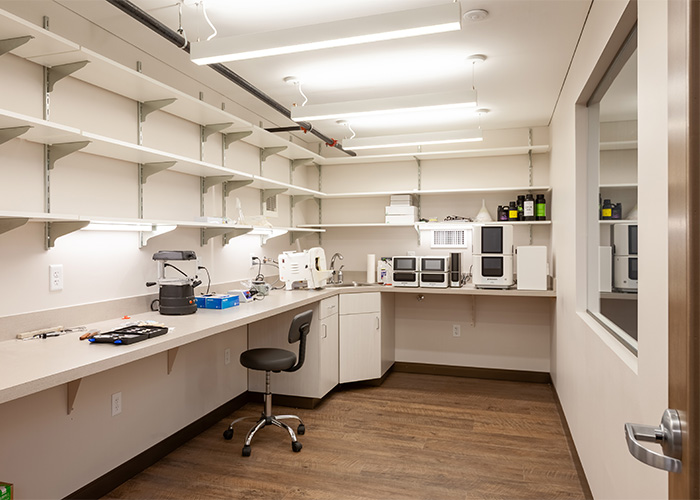 A well-organized laboratory with shelves holding bottles and containers, various equipment on countertops including a microscope and centrifuge, and a clean workspace with a wooden floor.