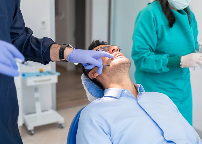 dentist and assistant examine top row of patient's teeth