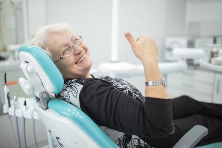 Person sitting in a dental chair, giving a thumbs-up gesture in a modern dental clinic.